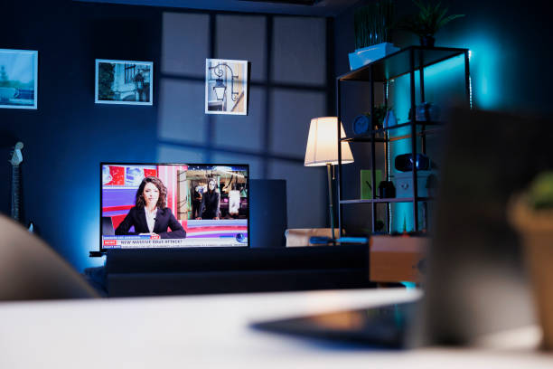 Empty stylish home studio interior illuminated with neon lights at night and artwork decorating the walls. Cozy apartment with TV running in background on news channel broadcast